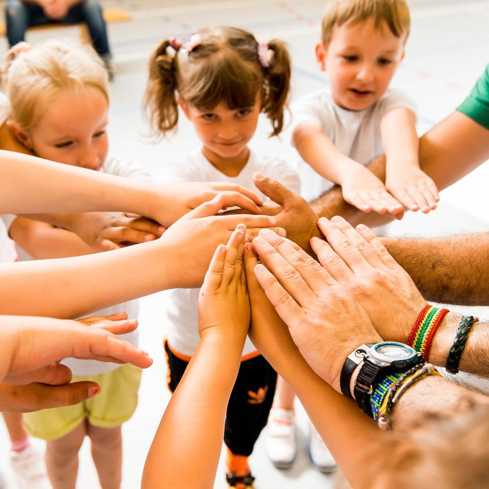 Kinder und Erwachsene legen ihre Hände in einem Kreis zusammen, symbolisieren Zusammenarbeit und Gemeinschaft.