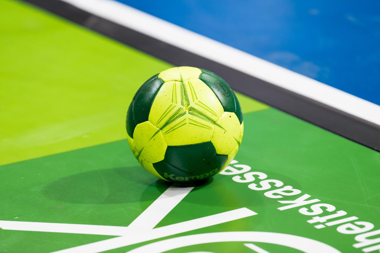 Grüner und gelber Handball liegt auf einer grünen Spielfläche mit weißem Schriftzug.