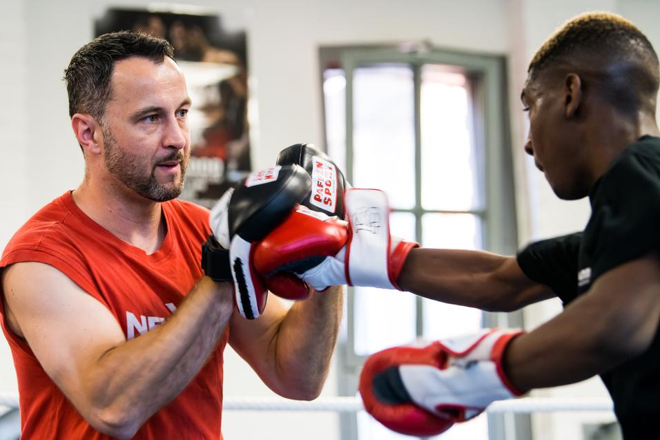 Trainer überwacht das Boxtraining eines Schülers, beide tragen Boxhandschuhe in einem Trainingsraum.