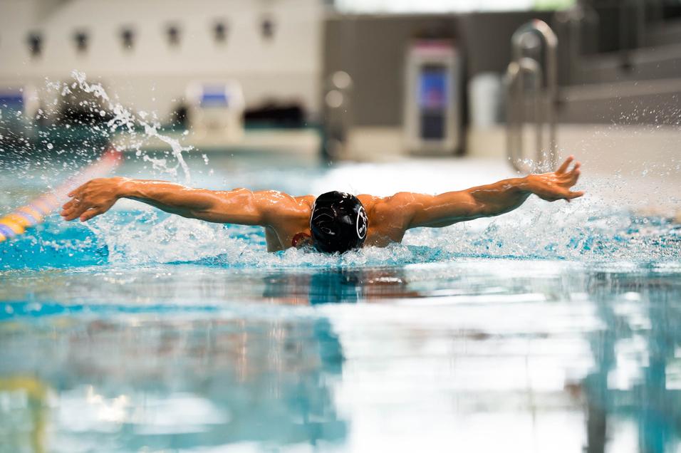 Schwimmer bei der Schmetterlingsbewegung im Wasser, Arme weit ausgebreitet, Spritzer um ihn herum.